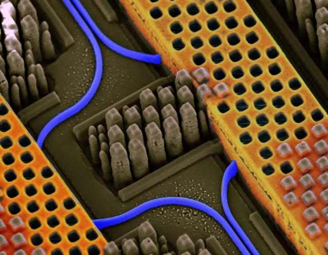 Angled view of a portion of an IBM chip showing blue optical waveguides transmitting high-speed optical signals and yellow copper wires carrying high-speed electrical signals